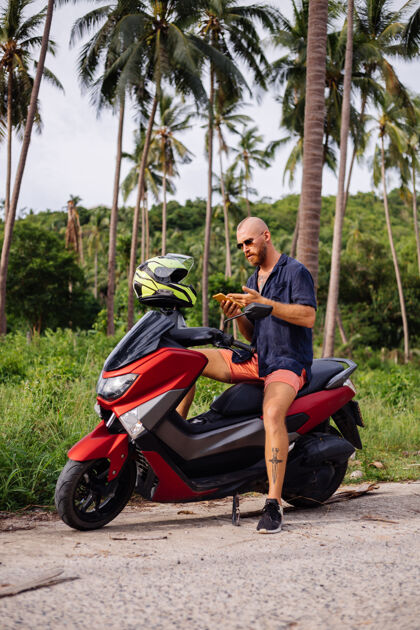 夏天在热带丛林的田野上纹着红色摩托车的壮汉服务人时尚