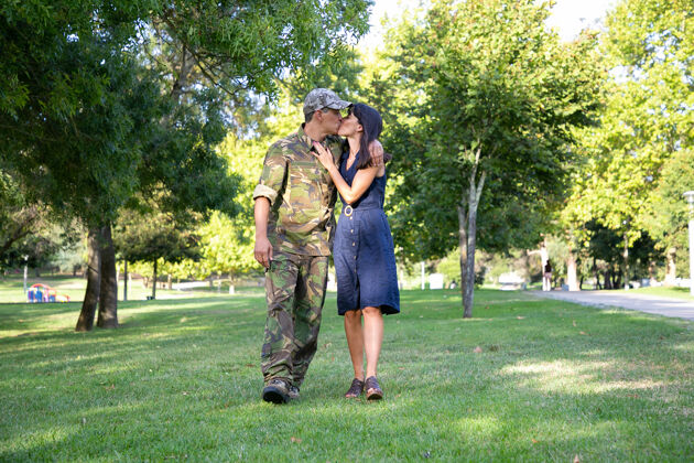 公园一对可爱的白种人在公园的草坪上拥抱 亲吻 散步身着军装的中年士兵 拥抱着他美丽的妻子家庭团聚 周末回家的概念帽子会议团聚