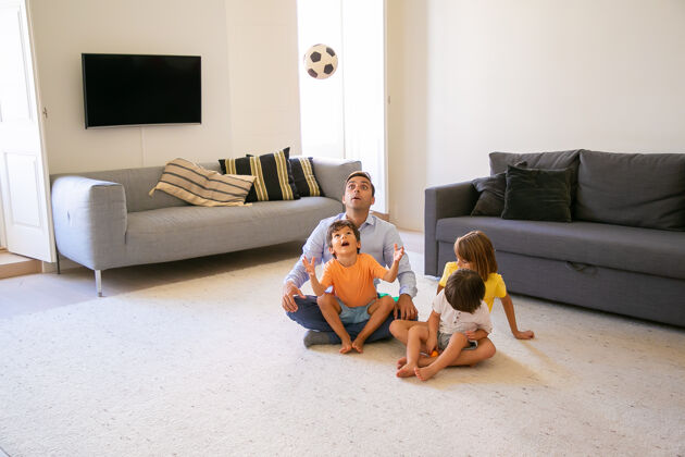 沙发爸爸和孩子们坐在地毯上玩耍可爱的顽皮男孩扔球看球可爱的孩子和爸爸在家玩童年 游戏和父亲的概念游戏小地毯
