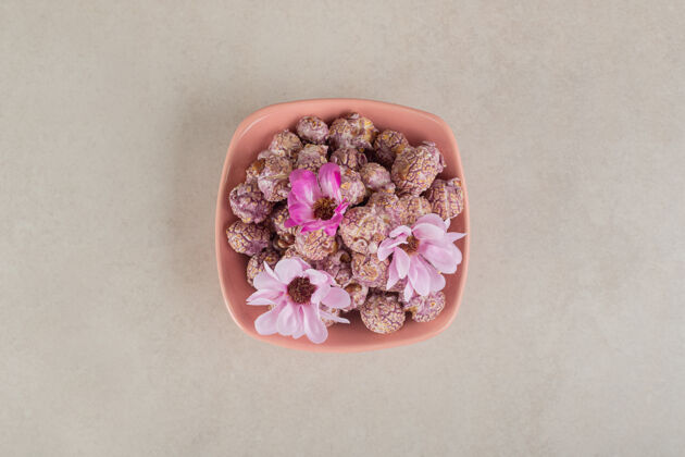 天然的满满一碗涂着糖果的爆米花 上面放着花 放在大理石上食物花顶视图