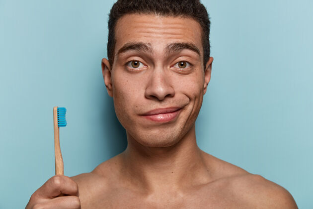 浴室皮肤健康 身体强壮 拿着牙刷 早上要做卫生程序 站在蓝色墙壁上的年轻人的特写镜头卫生 牙齿护理和美容概念卫生外观卫生