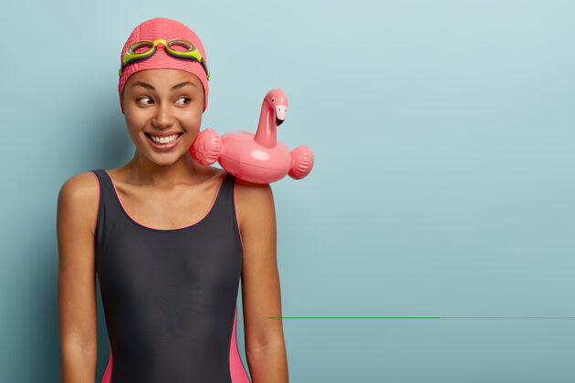 跳水深色皮肤的运动型苗条女性 穿着泳衣 有粉红色火烈鸟形状的游泳圈 头戴护目镜 在现代休闲中心闲暇 准备游泳积极休息度假村泳衣放松