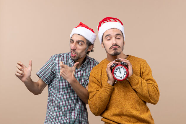 眼睛前视图两个圣诞老人一个眨眼 另一个拿着一个闹钟 眼睛闭着 背景是米色的闹钟男人男人