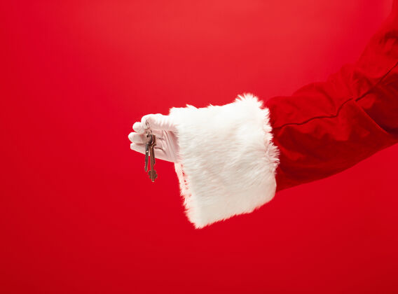 场合圣诞老人的手拿着公寓或车钥匙作为礼物放在红色欢乐公寓结