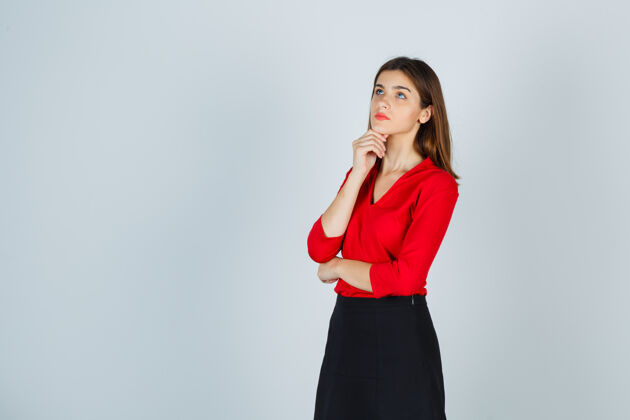 姿势年轻的女士站在思考的姿势 在红色上衣的拳头支撑下巴思考情感肖像