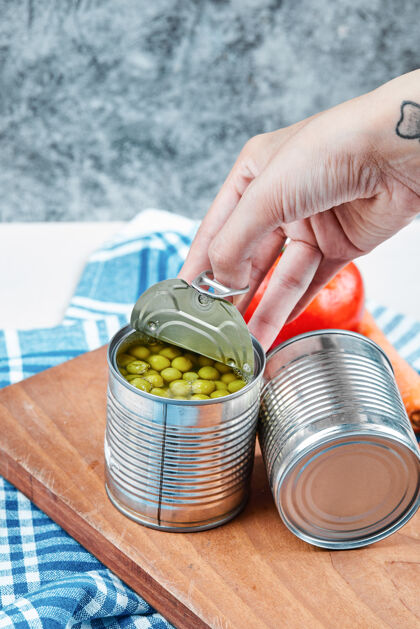 西红柿手拿一罐煮青豌豆放在一张白色的桌子上 桌子上放着蔬菜和桌布大理石滋补手