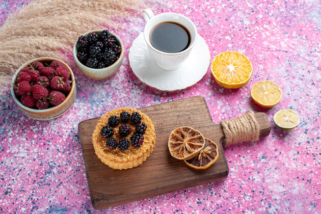 饮料半俯视图：在浅粉色背景上 用一杯茶蛋糕 在小罐子里放上覆盆子和黑莓水果浅粉色食品
