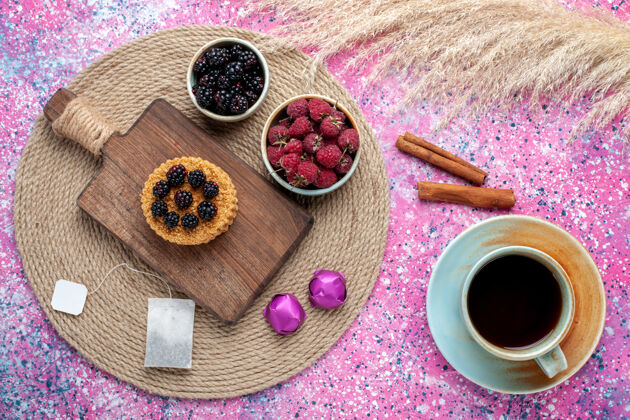 化妆品顶视图的小蛋糕与不同的浆果和茶杯在粉红色的表面刷子脸粉采购产品食物