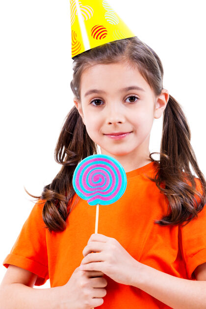 女性身着橙色t恤 戴着彩色糖果的派对帽的可爱小女孩的肖像-白色隔离庆祝漂亮高兴