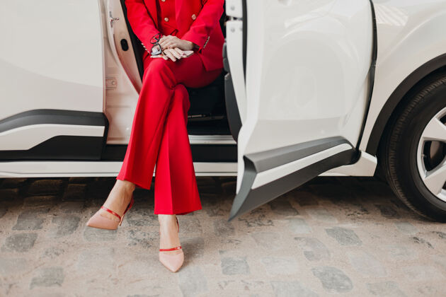 女士穿着高跟鞋和手拿着电话的性感富商美女穿着红色西装在白色汽车里摆姿势女人女商人电话