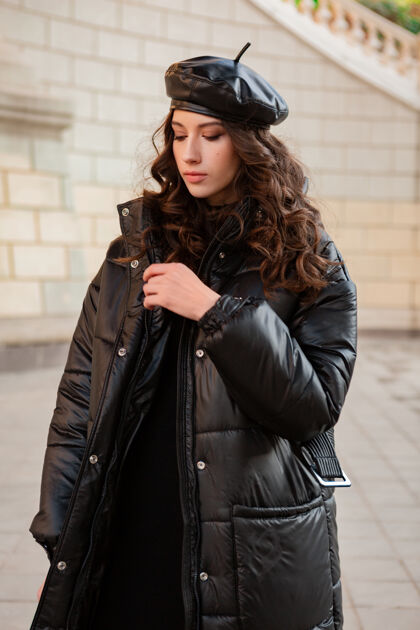 漂亮时尚女人摆出冬秋时尚潮流黑色羽绒服和皮帽贝雷帽在美丽老街户外城市女人