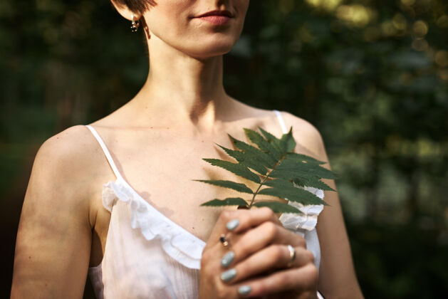 户外一个不可辨认的神秘年轻女子 短发 苍白的皮肤 独自在森林里行走 手里拿着一片绿色的蕨叶户外女人肖像