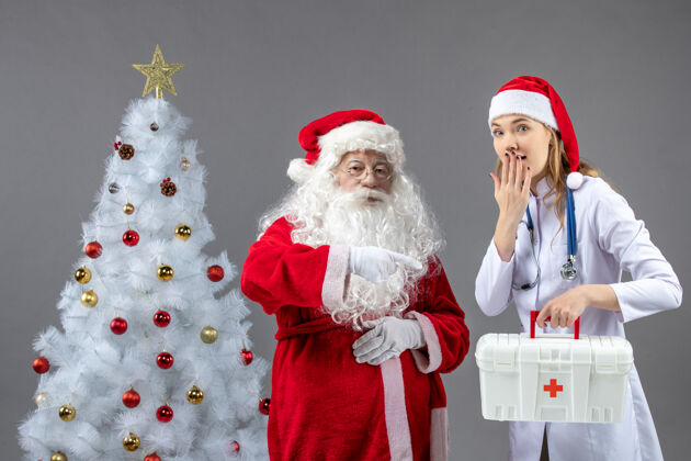医生圣诞老人和女医生的前视图 女医生拿着急救箱在灰色的墙上健康圣诞老人女性