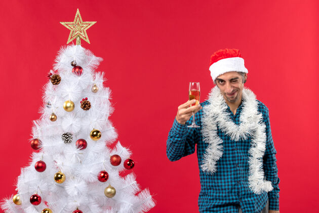 新年前夜圣诞心情自信坚定情绪化的年轻人戴着圣诞老人的帽子 在圣诞树旁举起一杯葡萄酒庆祝决心礼物