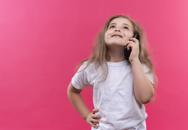 白色仰望着穿着白色t恤的小女生讲电话把她的手放在屁股上孤立的粉红色背景电话手小