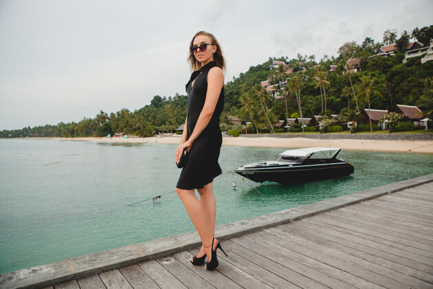 豪华奢华性感迷人的女人穿着黑色礼服在豪华度假酒店的码头上摆造型 戴着墨镜 暑假 热带海滩魅力户外船