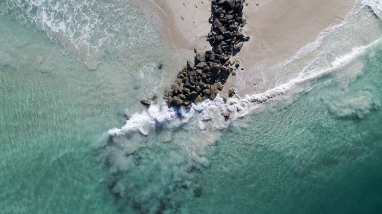 天空鸟瞰海浪打破了海滩上的岩石堆码头港口岩石