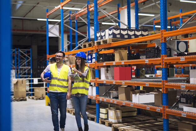 主管一群戴着安全帽和反光夹克的仓库工人在高货架和货物之间的过道里醒来微笑安全帽工作