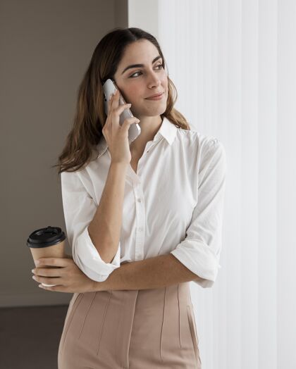 专业人士优雅的女商人一边拿着咖啡杯一边打电话女士垂直杯子