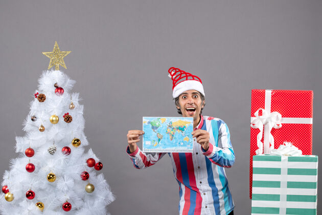 男人前视图笑脸人睁大眼睛拿着地图靠近白色圣诞树 并提出了复制空间有趣笑男人抱
