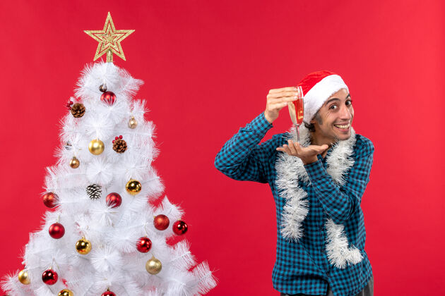 股票圣诞心情快乐的年轻人戴着圣诞老人的帽子 穿着蓝色的衬衫 在圣诞树旁举起一杯葡萄酒葡萄酒香槟白色