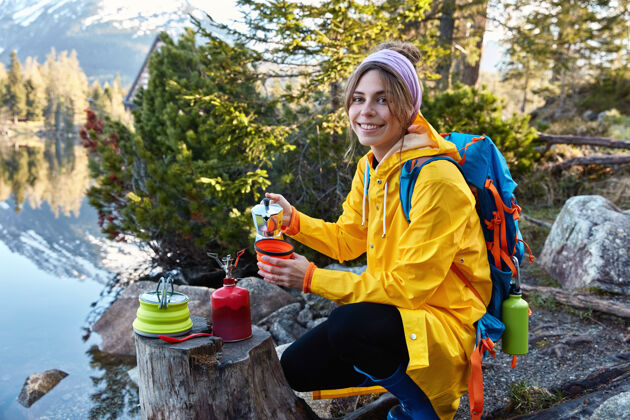 举行高兴的女游客从咖啡机里倒上热腾腾的芳香饮料 进行野营探险便携式饮料女