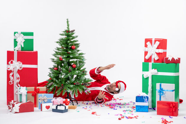 圣诞树圣诞老人躺在圣诞树后面 白色背景上的礼物旁 节日气氛热烈谎言圣诞老人圣诞老人