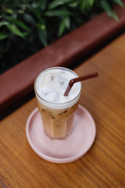 棕色在绿色灌木丛的夏日咖啡馆里 粉红色的架子上放着一杯冰拿铁清凉红茶全麦