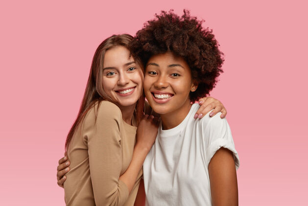 积极照片中两位年轻貌美的模特站得很近 拥抱并享受在一起的感觉 穿着休闲服 模特过了粉色的空间多样化多元文化快乐