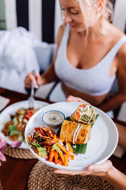 营养在夏日咖啡厅自然采光下享用色彩缤纷的健康素食沙拉的女士素食菜肴模特