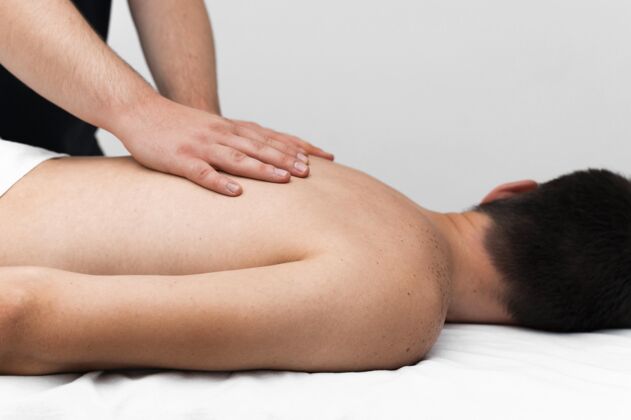 损伤理疗师按摩男子背部的侧视图背部医学运动