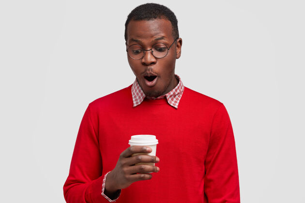 胡茬昏迷的黑人青年喝咖啡休息 听到谈话者的惊人消息 拿着一次性杯子 屏住呼吸 穿上红色毛衣经理惊讶饮料
