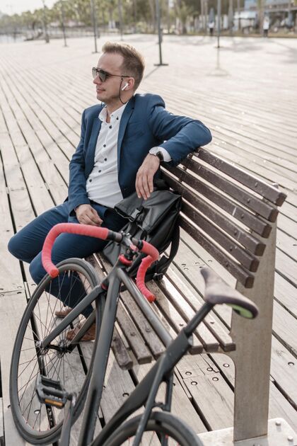 骑戴太阳镜的男人坐在自行车旁边的长凳上享受活跃的骑自行车的