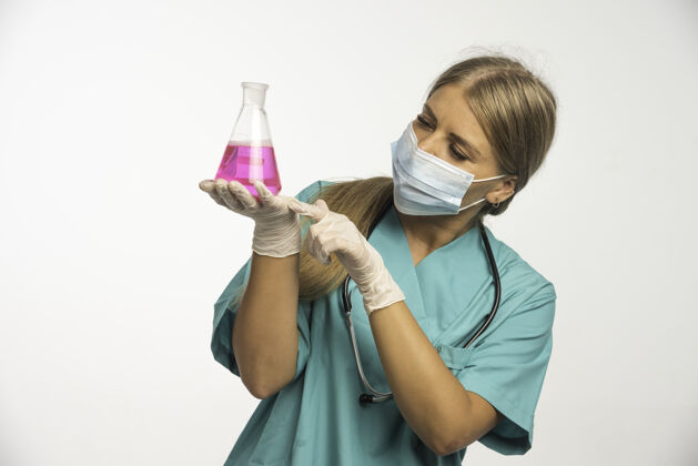 研究金发女医生 穿着蓝色制服 脖子上戴着听诊器 戴着口罩 手里拿着一个化学瓶服装演示制服