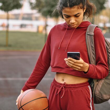 爱好一个女人拿着一个篮球在户外看手机运动装年轻比赛