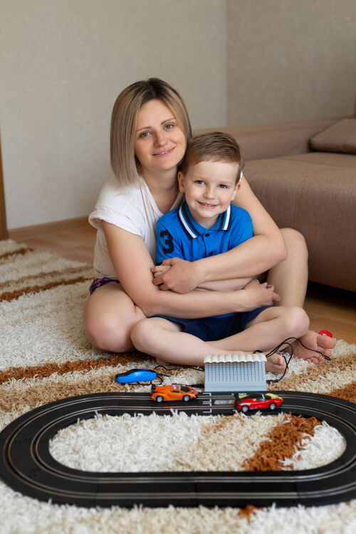 儿子妈妈和小儿子在家里的地毯上玩赛车 玩得开心又搂抱爱轨道童年