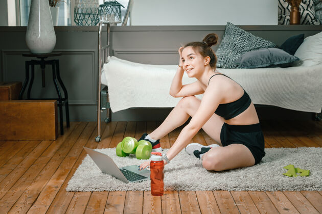 活动特写镜头中 一位身穿运动服的年轻女子躺在家里的地板上 通过笔记本电脑（一个社交网络）观看电影和学习形状笔记本电脑训练