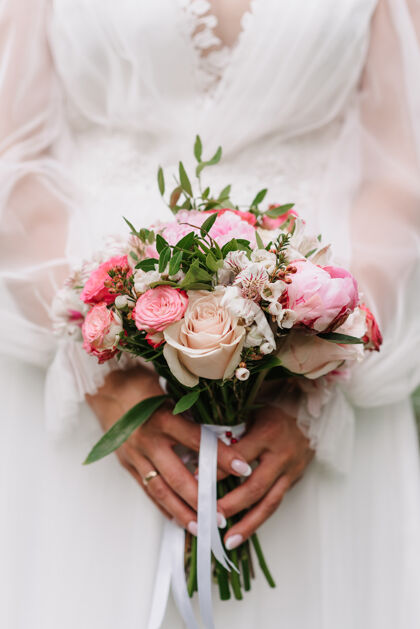 婚礼婚礼花束的白色和粉色玫瑰和牡丹在新娘的手中 背景是一件白色的礼服礼服芽特写