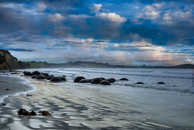 积云在达尼丁海滩及其标志性的巨石构造上 戏剧性的忧郁蓝色云景反射出蓝色色调坐着身体岩石