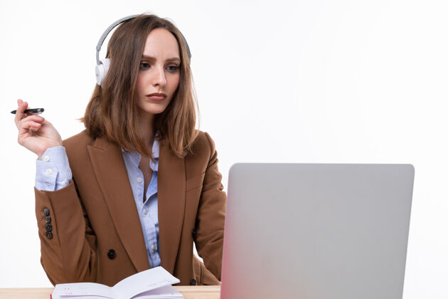 工人在工作场所 一位身着棕色西装的年轻女士正在一台头戴耳机的笔记本电脑前工作年轻行政漂亮