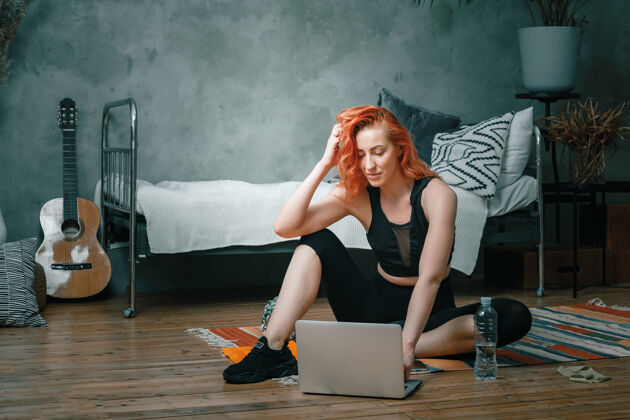 电脑特写镜头中 一位身穿运动服的年轻女子躺在家里的地板上 通过笔记本电脑（一个社交网络）观看电影和学习女性保健笔记本电脑锻炼
