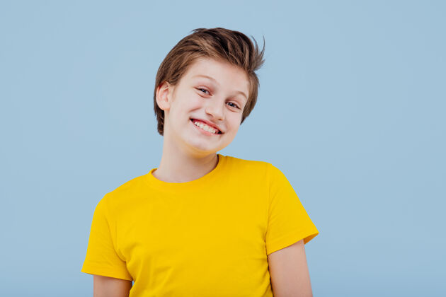 男孩微笑的男孩 穿着黄色t恤隔离在蓝色的墙上 复制空间小随意孩子