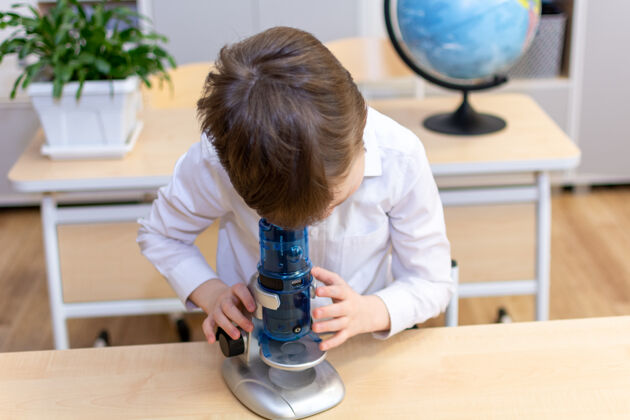 男孩一个穿着白衬衫的7-8岁男孩透过显微镜看高质量的照片好智力显微镜