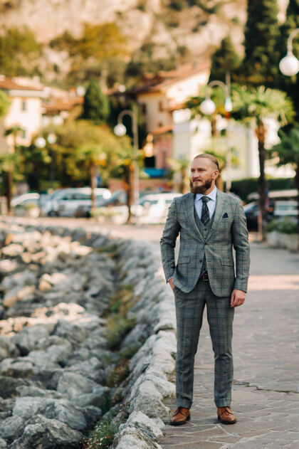 时尚在意大利托博勒附近的阿尔卑斯山的背景下 一个留着胡子的男人穿着一套严格的灰色三件套西装灰色西装堤岸意大利