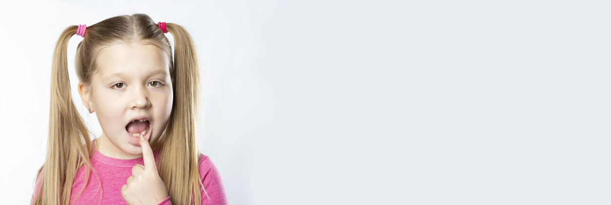 变化一位身穿粉色衣服 留着金色长发的白人小女孩在灯光背景下展示了她嘴里的乳牙牙齿卫生概念牙科孩子小