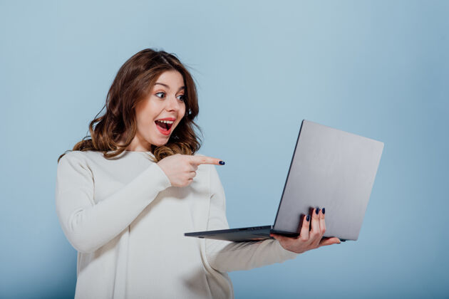 快递快乐的加号女士指着笔记本电脑后 发现在互联网上对蓝色墙慷慨提供小工具购买兴奋