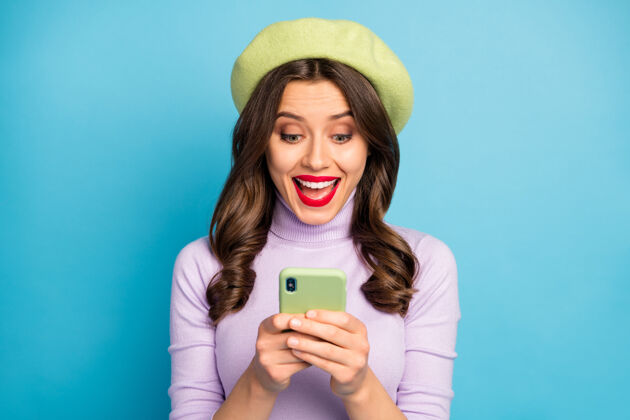 聪明特写照片兴奋的女孩沉迷社交网络用户阅读智能手机难以置信的通知尖叫哇omg穿时尚时尚的紫绿色衣服隔离蓝色墙壁秋天欢乐手机