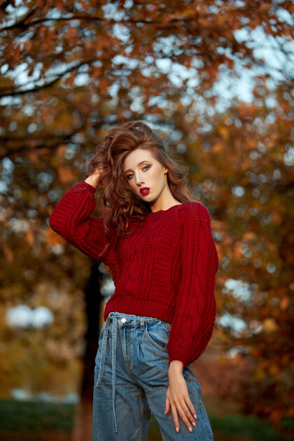 毛衣穿着红毛衣的红发女青年在公园里散步晚霞下一位时尚红发女子的秋美写真户外散步休闲