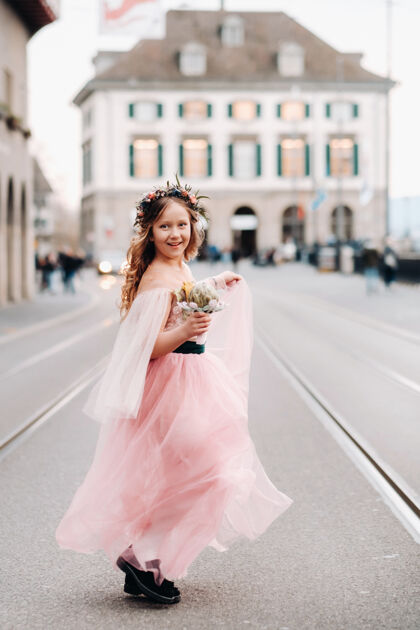 美丽一个穿着粉色公主裙的小女孩手里拿着一束花束 走在巴黎古城苏黎世肖像一个穿着粉色裙子的女孩在瑞士的城市街道上公主装衣服爱