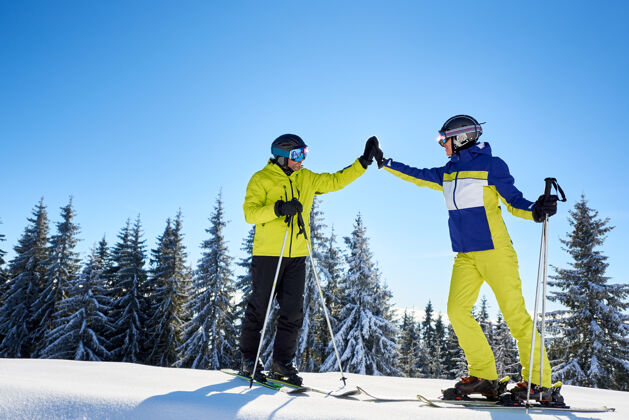 男人男女滑雪者在晴朗的蓝天下互相击掌成功地滑雪到山顶全长生活方式家庭度假